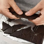 Carré de chocolat noir posé sur une table avec une tasse de café, illustration du meilleur moment pour manger du chocolat noir