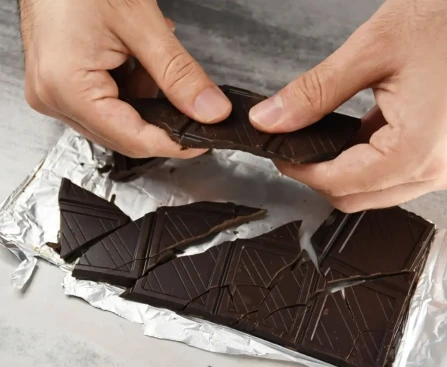 Carré de chocolat noir posé sur une table avec une tasse de café, illustration du meilleur moment pour manger du chocolat noir