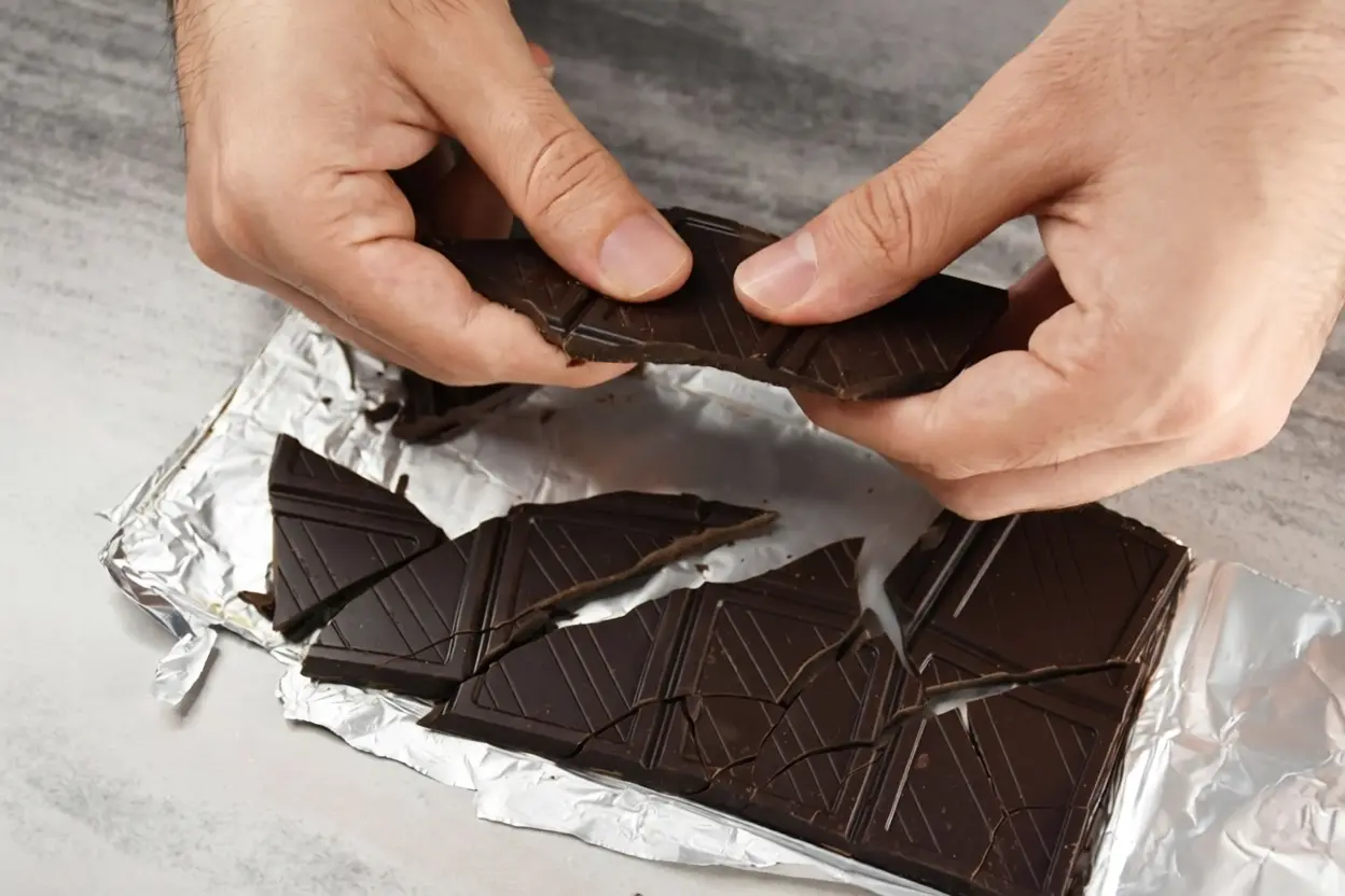 Carré de chocolat noir posé sur une table avec une tasse de café, illustration du meilleur moment pour manger du chocolat noir