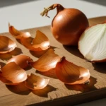 Épluchures d'oignon dorées sur une planche en bois à côté d'un oignon coupé